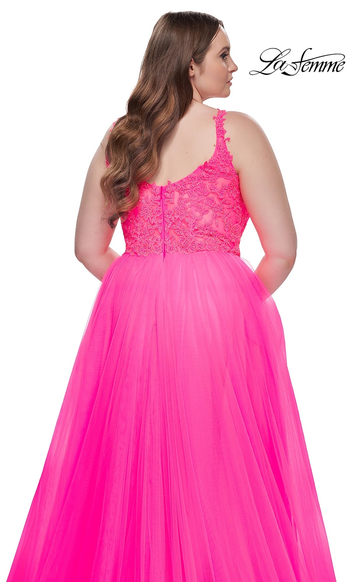 A woman is seen from the back wearing the La Femme Long Prom Dress 31394, a floor-length plus-size ball gown in bright pink with thin shoulder straps, an embroidered lace bodice, and a zipper closure.